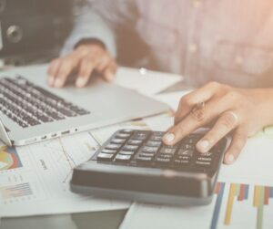 Close-up of hands using a calculator with mortgage paperwork spread across a desk